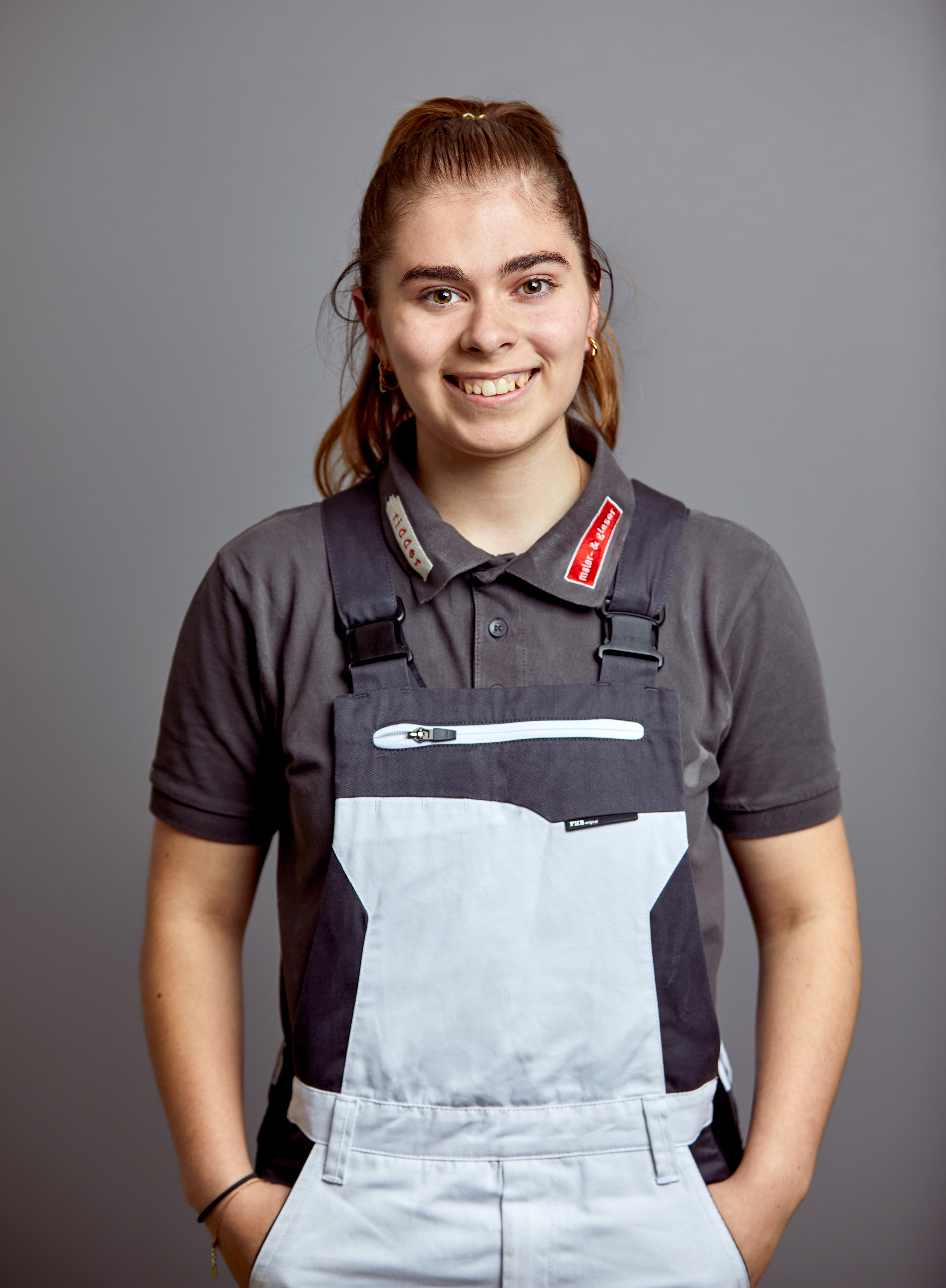 Portrait junge Frau im Maleranzug, lächelt, grauer Hintergrund